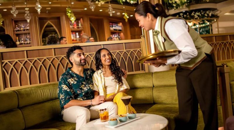 A couple enjoys cocktails and appetizers while chatting with a Cast Member at a cozy dining table