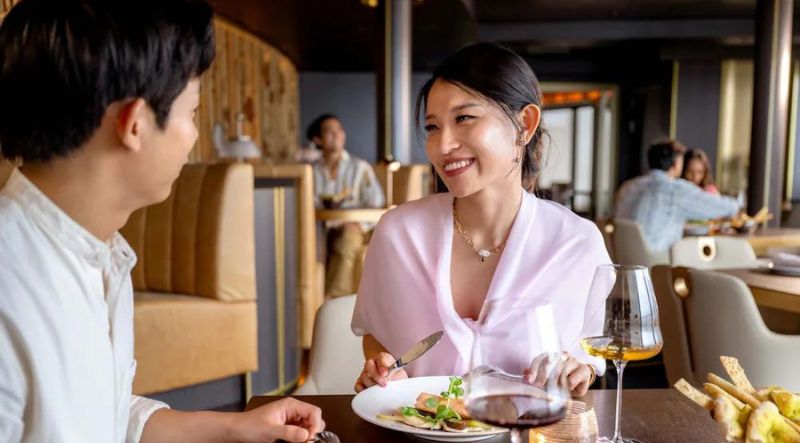 A couple sits at a dining table, their meal consisting of entrees, glasses of wine, and breadsticks