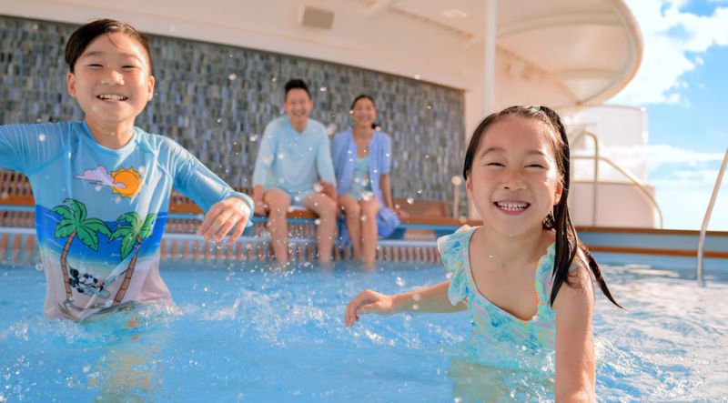 Two young children splash and play in a pool as their parents supervise from the edge